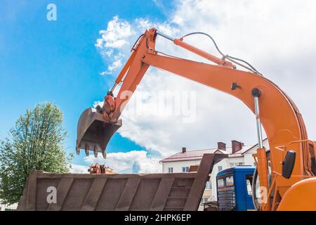 Aushubarbeiten. Der Eimer des Traktors lädt den Boden mit einer Schaufel in die Rückseite eines Muldenkipper auf der Baustelle. Stockfoto