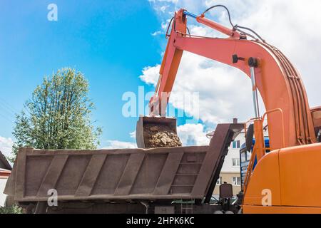 Aushubarbeiten. Der Eimer des Traktors lädt den Boden mit einer Schaufel in die Rückseite eines Muldenkipper auf der Baustelle. Stockfoto