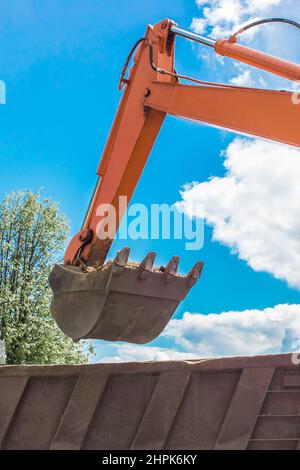 Aushubarbeiten. Der Eimer des Traktors lädt den Boden mit einer Schaufel in die Rückseite eines Muldenkipper auf der Baustelle. Stockfoto