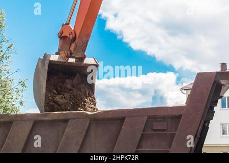 Aushubarbeiten. Der Eimer des Traktors lädt den Boden mit einer Schaufel in die Rückseite eines Muldenkipper auf der Baustelle. Stockfoto