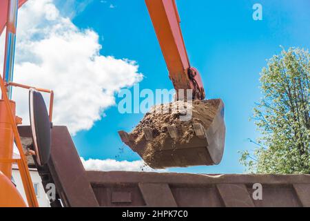Aushubarbeiten. Der Eimer des Traktors lädt den Boden mit einer Schaufel in die Rückseite eines Muldenkipper auf der Baustelle. Stockfoto