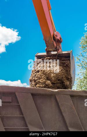 Aushubarbeiten. Der Eimer des Traktors lädt den Boden mit einer Schaufel in die Rückseite eines Muldenkipper auf der Baustelle. Stockfoto