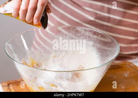 Nahaufnahme Frau siebt Weizenmehl durch ein Sieb in eine Rührschüssel zur Teigvorbereitung für Kuchen und Backwaren auf schwarzem Hintergrund. Den Teig für hausgemachtes Gebäck kneten. Stockfoto