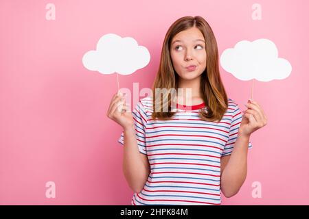 Foto von unsicher kleine braune Frisur Mädchen halten Wolken suchen leeren Raum tragen gestreiftes T-Shirt isoliert auf rosa Hintergrund Stockfoto