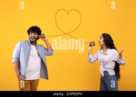 Liebes Lied. Liebevolle indische Dame sendet ihrem Freund eine romantische Nachricht über ein Zinntelefon auf gelbem Hintergrund Stockfoto