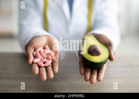 Gesundheits- und Diät-Konzept. Ernährungsberaterin hält Haufen von Pillen und die Hälfte von Avocado, arbeitet in der Klinik, Nahaufnahme Stockfoto