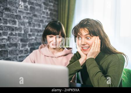 Zwei junge Frauen erhalten gute Nachrichten über das Internet oder die Lotterie beim Betragen eines Laptops. Glücklich überrascht Mädchen bekommt positive Emotion. Stockfoto