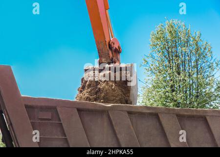 Aushubarbeiten. Der Eimer des Traktors lädt den Boden mit einer Schaufel in die Rückseite eines Muldenkipper auf der Baustelle. Stockfoto