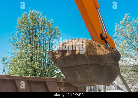 Aushubarbeiten. Der Eimer des Traktors lädt den Boden mit einer Schaufel in die Rückseite eines Muldenkipper auf der Baustelle. Stockfoto
