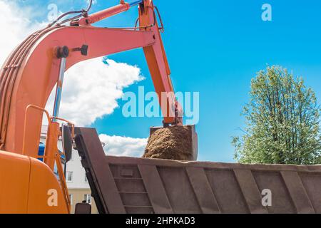 Aushubarbeiten. Der Eimer des Traktors lädt den Boden mit einer Schaufel in die Rückseite eines Muldenkipper auf der Baustelle. Stockfoto