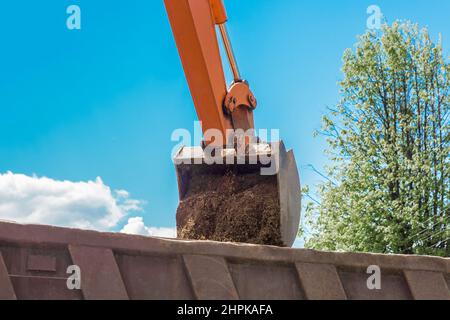 Aushubarbeiten. Der Eimer des Traktors lädt den Boden mit einer Schaufel in die Rückseite eines Muldenkipper auf der Baustelle. Stockfoto