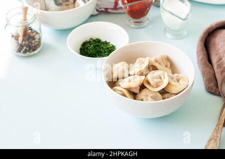 Hausgemachte Fleischknödel – traditionelle russische Pelmeni-Platte, gefüllt mit Hackfleisch, serviert in einer weißen Schüssel. Stockfoto