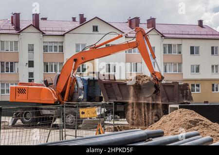 Aushubarbeiten. Der Eimer des Traktors lädt den Boden mit einer Schaufel in die Rückseite eines Muldenkipper auf der Baustelle. Stockfoto