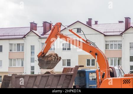 Aushubarbeiten. Der Eimer des Traktors lädt den Boden mit einer Schaufel in die Rückseite eines Muldenkipper auf der Baustelle. Stockfoto