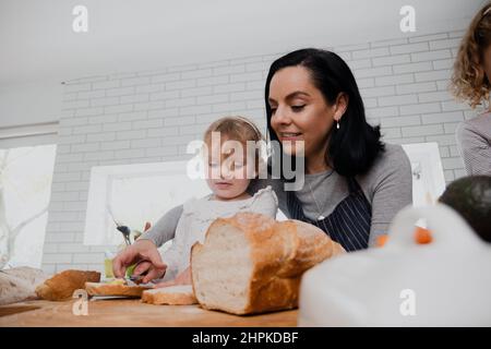 Kaukasische Mutter und Tochter kochen in der Küche und machen Mittagessen für die Familie beim Schneiden von Brot Stockfoto