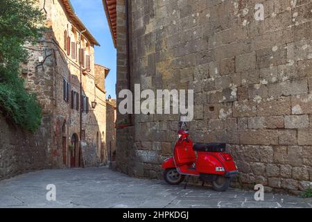 Das alte rote Moto lehnte sich an die Schattenmauer eines alten großen Backsteingebäudes in Monticchiello. Toskana, Italien Stockfoto