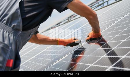 Beschnittene Ansicht von Menschenhänden in Arbeitshandschuhen, die Photovoltaik-Solarmodule montieren. Arbeiter Montage von Solarmodulen zur Stromerzeugung durch Photovoltaik-Effekt. Konzept für erneuerbare Energiequellen. Stockfoto