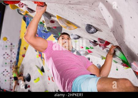 Männliche alpinist Üben indoor Klettern an künstlichen Boulder ohne Sicherheitsgurte Stockfoto