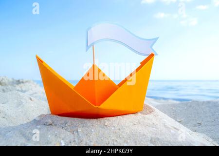 Orange Papier Boot auf Sandy Seashore Nahaufnahme kleines Boot aus Papier auf dem Hintergrund Stockfoto