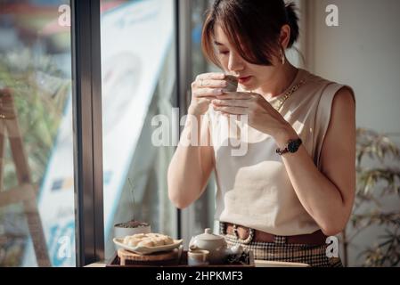 Eine Asiatin schnüffelt Tee und hat einen Satz gerösteten Mitarashi Dango vor sich. Stockfoto