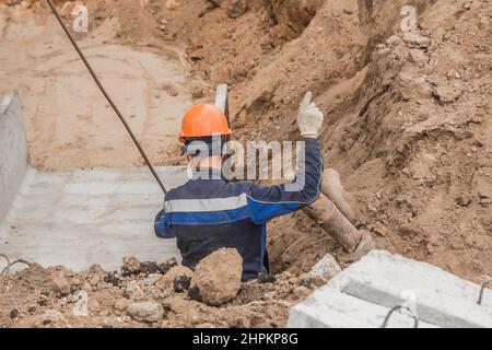 Bauarbeiter in Schutzhelm und Overalls Gesten während der Arbeit in einem Industriegebiet einer Baustelle. Stockfoto