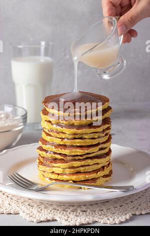 Küchenchef gießt kondensierte Kokosmilch auf Kokosmehl-Pfannkuchen, veganes Essen, grauer Hintergrund, vertikales Format Stockfoto