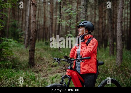 Ältere Biker, die am Herbsttag im Wald im Freien im Fahrradhelm aufsetzen. Stockfoto