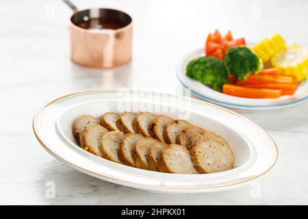 Hackbraten mit würzigem Glasur in Scheiben geschnitten auf einem Teller, zermahlenes Rindfleisch und Schweinefleisch, serviert mit gedämpftem Gemüse, auf dem weißen Tisch Stockfoto