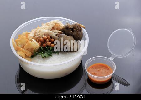 Bubur Ayam oder indonesischer Reisporridgew mit geschreddertem Huhn. Serviert mit Kerukpuk (Cracker), Sojasoße, gebratenen Sojabohnen und Sambal. Isoliert auf Bla Stockfoto