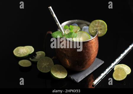 Kalter Moscow Mule Alkoholischer Cocktail in Kupferbecher mit Eis, Minze und Zitrone auf schwarzem Stein Tischhintergrund. Nahaufnahme, Kopierbereich Stockfoto