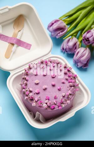Lunchbox aus Kunststoff mit leckerem Bento-Kuchen und Blumen auf blauem Hintergrund Stockfoto