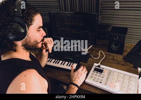 Junger mann aus dem lateinischen Kaukasus in seinem Heimstudio, mit Keyboards, Computer und Midi-Controller, Musik denken und produzieren, Konzept der Musikindustrie. Stockfoto