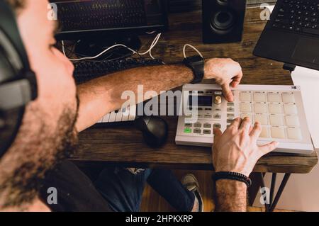 Aus erster Person betrachtet, wie der kaukasische Mann in seinem Heimstudio Musik kreist und Beats mit Midi-Controller, Keyboards, Computer und Notebook produziert, Musik Stockfoto