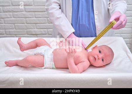 Der Arzt misst das Wachstum eines Neugeborenen. Eine Krankenschwester in Uniform überprüft den Umfang des Kopfes und des Unterleibs des Kindes Stockfoto