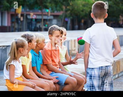 Jungs und Mädchen sitzen und spielen mit Ball im Freien Stockfoto