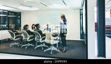 Eine kluge Geschäftsfrau, die in einem Sitzungssaal eine finanzielle Präsentation vorführt. Selbstbewusste Geschäftsfrau, die ihren Kollegen statistische Details vorstellt. Gruppe von Stockfoto