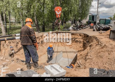 Weißrussland, Region Minsk - 20. Mai 2020: Ein Vorarbeiter in Overalls und ein Schutzhelm steuert den Arbeitsprozess des Hebens von Betonkonstruktionen am Stockfoto