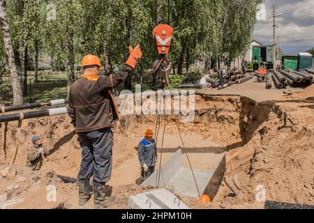 Weißrussland, Region Minsk - 20. Mai 2020: Ein Vorarbeiter in Overalls und ein Schutzhelm steuert den Arbeitsprozess des Hebens von Betonkonstruktionen am Stockfoto