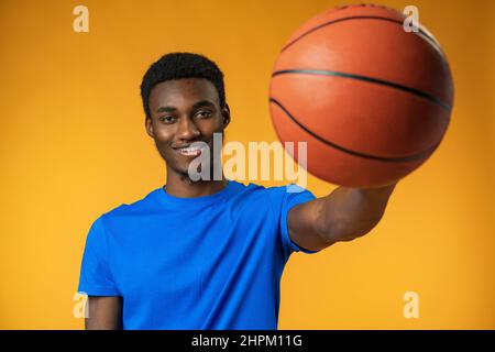 Porträt eines lächelnden jungen afroamerikanischen Mannes, der einen Basketball auf gelbem Hintergrund hält Stockfoto