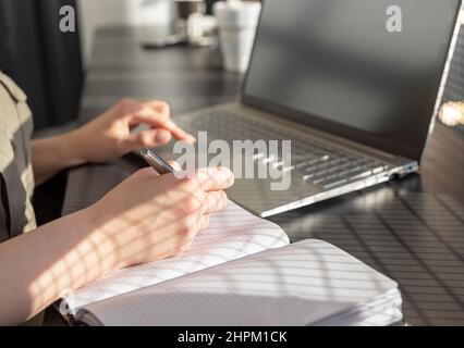 Frau nimmt sich Notizen in der Planerin und arbeitet im Café an einem Laptop. Online-Bildungs- und Arbeitskonzept. Nahaufnahme. Hochwertige Fotos Stockfoto