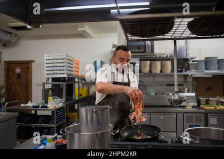 Reifer Koch, der gehackte Vehetagles in die Restaurantküche einfügt, um sie drinnen zu pfannen. Stockfoto