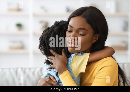 Fürsorgliche afroamerikanische Frau umarmt kleine Tochter, tröstet ihr verärgertes Kind, Nahaufnahme von liebevoller schwarzer Mutter Umarmung weibliches Kind zu Hause, L Stockfoto