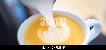 Barista gießt Milch in Espressokaffee, um Cappuccino und Latte Art zuzubereiten Stockfoto