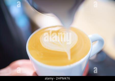 Barista gießt Milch in Espressokaffee, um Cappuccino und Latte Art zuzubereiten Stockfoto