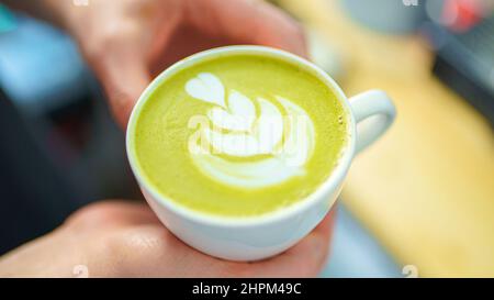 Barista hält eine Tasse Matcha Latte in den Händen Stockfoto