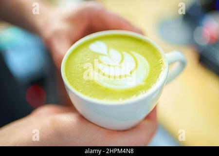 Barista hält eine Tasse Matcha Latte in den Händen Stockfoto