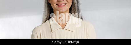 Porträt einer ziemlich grauhaarigen Frau in beiger Bluse auf hellem Hintergrund Stockfoto