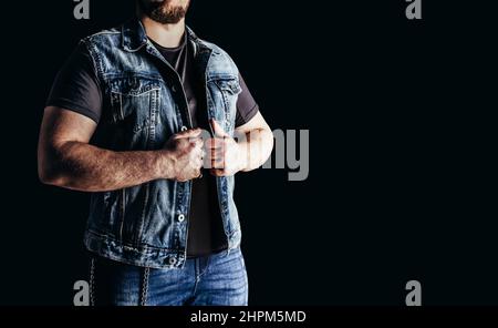 Foto eines Mannes in Jeans-Hemd und Jeans-Biker-Weste auf schwarzem Hintergrund. Stockfoto