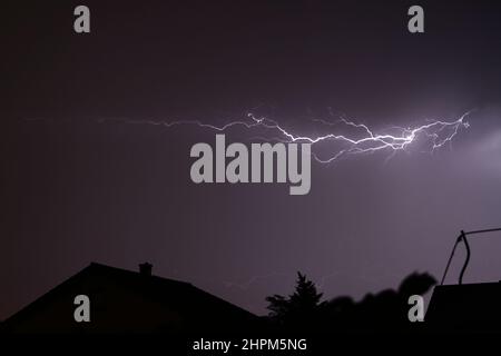 Blitze blitzen über einen stürmischen Nachthimmel mit Häusern Stockfoto