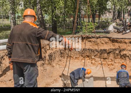 Weißrussland, Region Minsk - 20. Mai 2020: Ein Vorarbeiter in Overalls und ein Schutzhelm steuert den Arbeitsprozess des Hebens von Betonkonstruktionen am Stockfoto